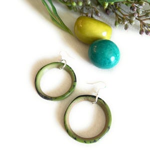 Puede incluir: Un par de pendientes de aro verdes con un diseño de mármol blanco y negro. Los pendientes están hechos de madera y tienen ganchos de plata.