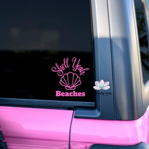 May include: Pink vinyl decal with the text "Shell Yeah Beaches" and a pink seashell graphic. The decal is on the back window of a pink Jeep.