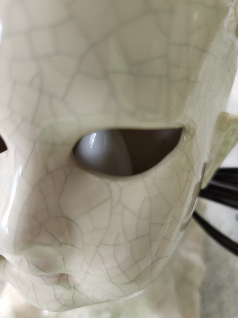 Puede incluir: Primer plano de una escultura de cer&aacute;mica de una cara con un ojo abierto. La escultura es de color blanquecino con un aspecto agrietado y envejecido. La cuenca del ojo es un vac&iacute;o oscuro y la oreja es visible en el lateral.