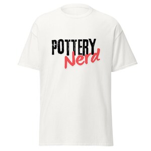 May include: White t-shirt with the words "POTTERY Nerd" printed on the front. The word "POTTERY" is in a bold, black font, and "Nerd" is in a cursive, red font with a shadow.