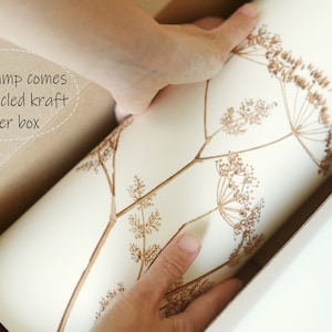 K&ouml;nnte beinhalten: Eine wei&szlig;e Papierbox mit braunem Blumenmuster wird aus einer gr&ouml;&szlig;eren braunen Kartonbox genommen. Der Text "Every lamp comes in a recycled kraft paper box" ist auf der Kartonbox sichtbar.