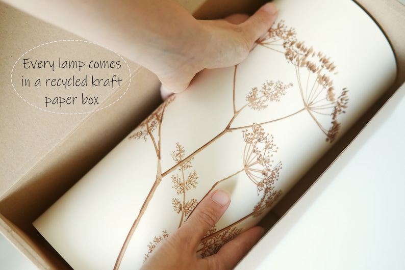 K&ouml;nnte beinhalten: Eine wei&szlig;e Papierbox mit braunem Blumenmuster wird aus einer gr&ouml;&szlig;eren braunen Kartonbox genommen. Der Text "Every lamp comes in a recycled kraft paper box" ist auf der Kartonbox sichtbar.