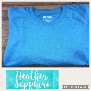 May include: A folded blue heather sapphire Gildan t-shirt. The Gildan brand name is visible on the shirt's tag.