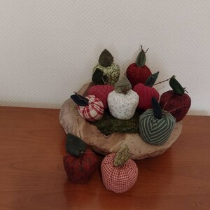 Könnte beinhalten: Eine Holzschale gefüllt mit handgefertigten Stoffäpfeln in verschiedenen Farben und Mustern, darunter Rot, Grün und Weiß. Die Äpfel sind in einer dekorativen Anordnung angeordnet.