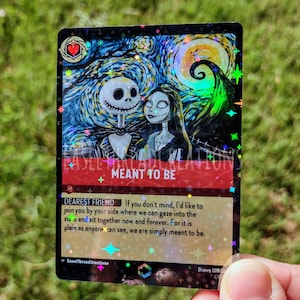 May include: A holographic card with a starry night sky background featuring Jack Skellington and Sally from the Nightmare Before Christmas movie. The card has the text "Meant to Be" and a quote from the movie: "If you don't mind, I'd like to join you by your side where we can gaze into the stars and sit together now and forever. For it is plain as anyone can see, we are simply meant to be."