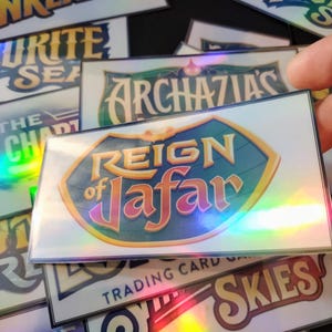 May include: A collection of holographic trading cards featuring various Disney characters and themes, including "Reign of Jafar", "The Archazias", "Into the Inklands", "Sky's the Limit", and "The Pirate Sea".