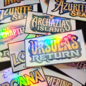 May include: A collection of holographic game cards with titles like "Into the Inklands", "Azurith Sea", "Archazia's Island", "Ursula's Return", "Orcana", and "Merging Skies".