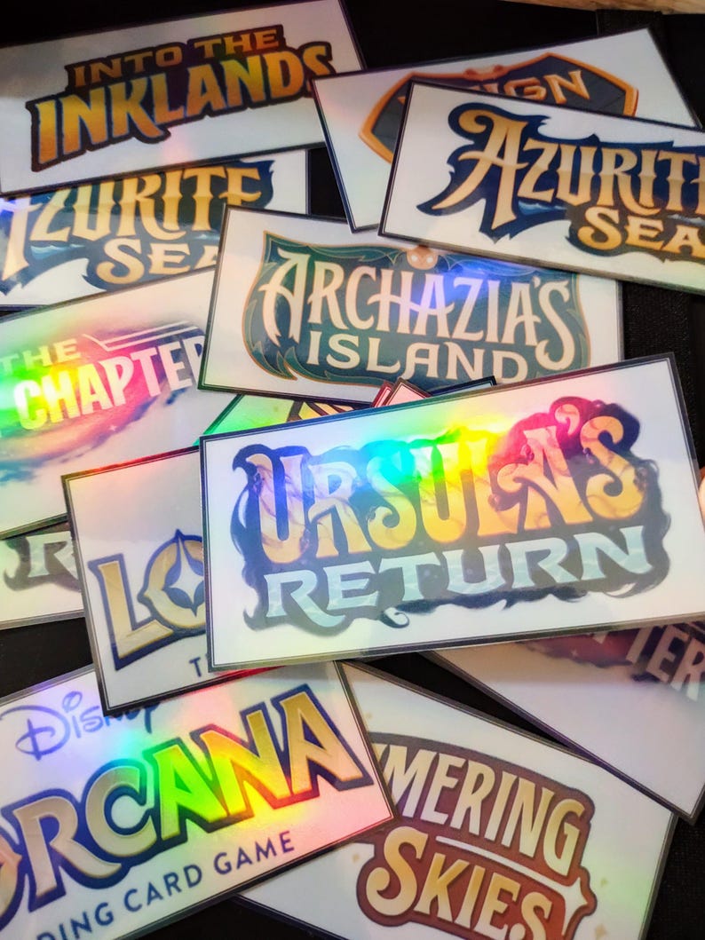 May include: A collection of holographic game cards with titles like "Into the Inklands", "Azurith Sea", "Archazia's Island", "Ursula's Return", "Orcana", and "Merging Skies".