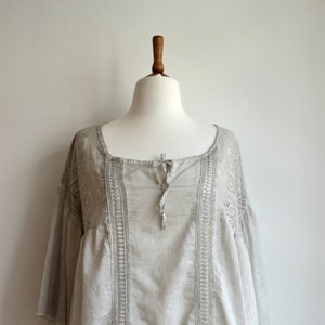 May include: A light gray cotton blouse with a lace trim and a tie at the neckline.