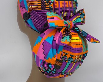 Puede incluir: Un gorro quirúrgico estampado de colores con una corbata de lazo. El gorro está hecho de tela con un diseño geométrico en tonos naranja, rosa, morado, azul, verde y negro.