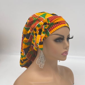 May include: A yellow, green, red, and black patterned satin bonnet with a bow on top. The bonnet is worn by a mannequin with silver earrings.
