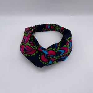 May include: A patterned headband with a dark blue background and a colorful floral design in pink, green, and blue. The headband is knotted at the front and has an elastic band at the back for a comfortable fit.