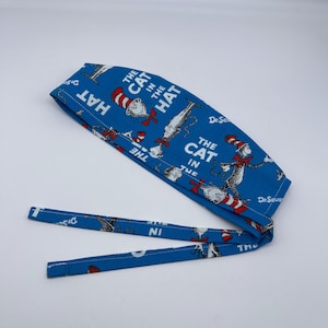 May include: Blue surgical scrub hat with adjustable ties. The hat features a repeating pattern of the Cat in the Hat from the Dr. Seuss book.
