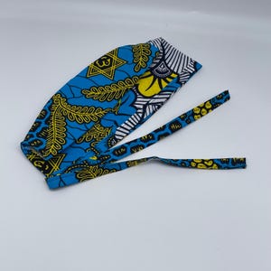 May include: A blue and yellow patterned surgical scrub hat with black and white accents. The hat has two long ties.