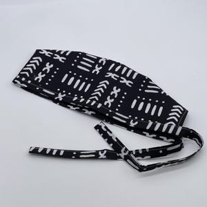 May include: Black and white patterned surgical scrub cap with a tie closure. The pattern features geometric shapes and lines.