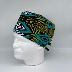Puede incluir: Un gorro de quirófano con un patrón geométrico negro, amarillo y turquesa. El gorro tiene un lazo en la parte posterior.