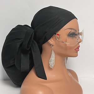 May include: A black satin sleep cap with a long tie. The cap is tied in a bun shape on top of the head. The model is wearing clear framed glasses with gold accents.