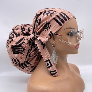 May include: A pink and black patterned surgical cap with a large bun, tied with a long tie. The cap is made of a soft, comfortable fabric and is designed to keep hair out of the way during surgery or other medical procedures.