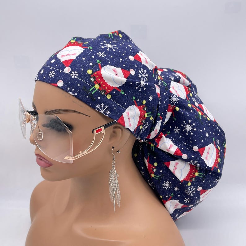 May include: A navy blue bouffant scrub cap with a Santa Claus and snowflake pattern. The cap is paired with clear, oversized rimless glasses with gold frames and a red accent. Silver feather earrings complete the look.
