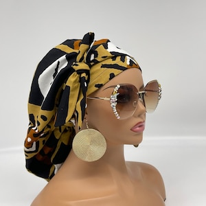 May include: A mannequin head is adorned with a patterned head wrap, large gold earrings, and oversized sunglasses. The sunglasses have a gold frame and are embellished with rhinestones. The head wrap features a black, white, and brown animal print.