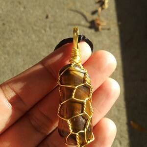 Puede incluir: Un colgante de ojo de tigre envuelto en alambre dorado con un cordón negro.