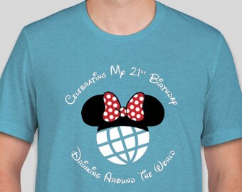 May include: A turquoise blue t-shirt with a white graphic of Mickey Mouse ears with a red bow and a globe with the text "Celebrating My 21st Birthday Drinking Around the World".