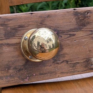 May include: A reclaimed wooden coat rack featuring four polished brass door knobs. The wood is a distressed brown colour, showing the natural grain. The knobs are symmetrically arranged, providing a practical and vintage-inspired storage solution.