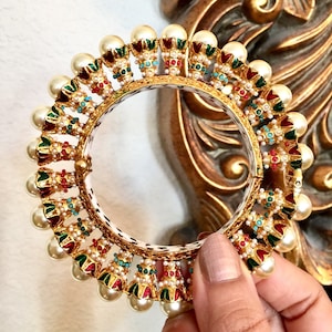 May include: A gold bangle bracelet with a decorative design of green, red, and blue enamel. The bracelet is adorned with white pearls.