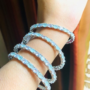 May include: Four silver bangles with light blue oval-shaped stones set in a continuous line around each bangle.