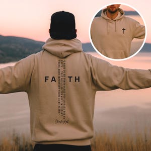 May include: Sand-colored hoodie with the word "FAITH" printed on the back in black, with a cross graphic. The hoodie also features a quote and a small cross on the front. The New Life Logo is at the bottom left.