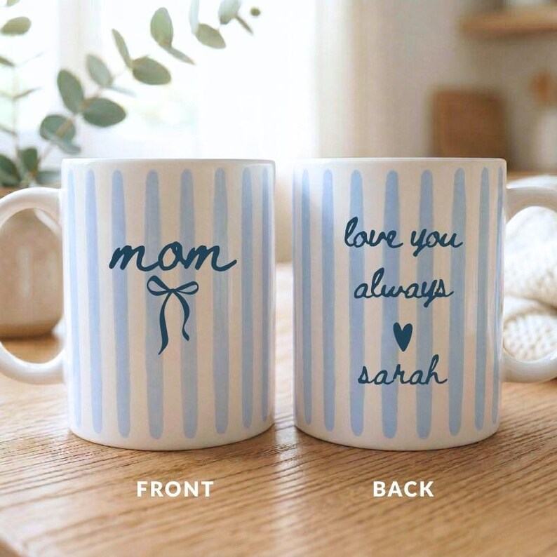 May include: A white ceramic mug with a black handle and the text "But First, Coffee" in a black, handwritten-style font. The mug is on a white surface.