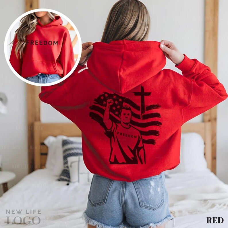 May include: A red hoodie with the word "FREEDOM" printed on the front and back. The back features a graphic of a person raising a fist in front of an American flag and a cross. The hoodie has a front pocket and a hood.