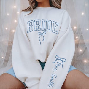 Bride Sweatshirt with blue Bow and the Custom Mrs. Last Name on sleeve. Perfect for an engagement or Something Blue before I do Gift or party.