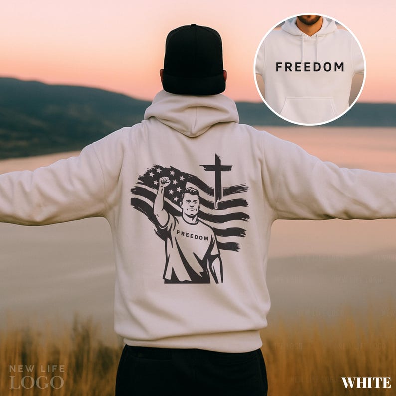May include: Cream-colored hoodie with the word "FREEDOM" printed on the front and back. The back features a graphic of a man raising his fist in front of an American flag and a cross. The hoodie is worn by a person wearing a black cap.