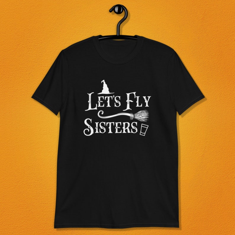 May include: Black t-shirt with white text that reads "Let's Fly Sisters" with a witch's hat and broom graphic.