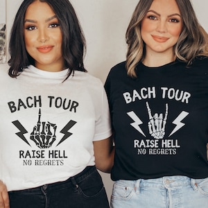 May include: Two women wearing black and white t-shirts with the text "Bach Tour" and a skeleton hand graphic. The text below the graphic says "Raise Hell No Regrets".