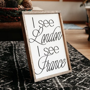 May include: A wooden framed sign with white background and black text that reads "I see London I see France". The sign is sitting on a black and white patterned rug in a living room.