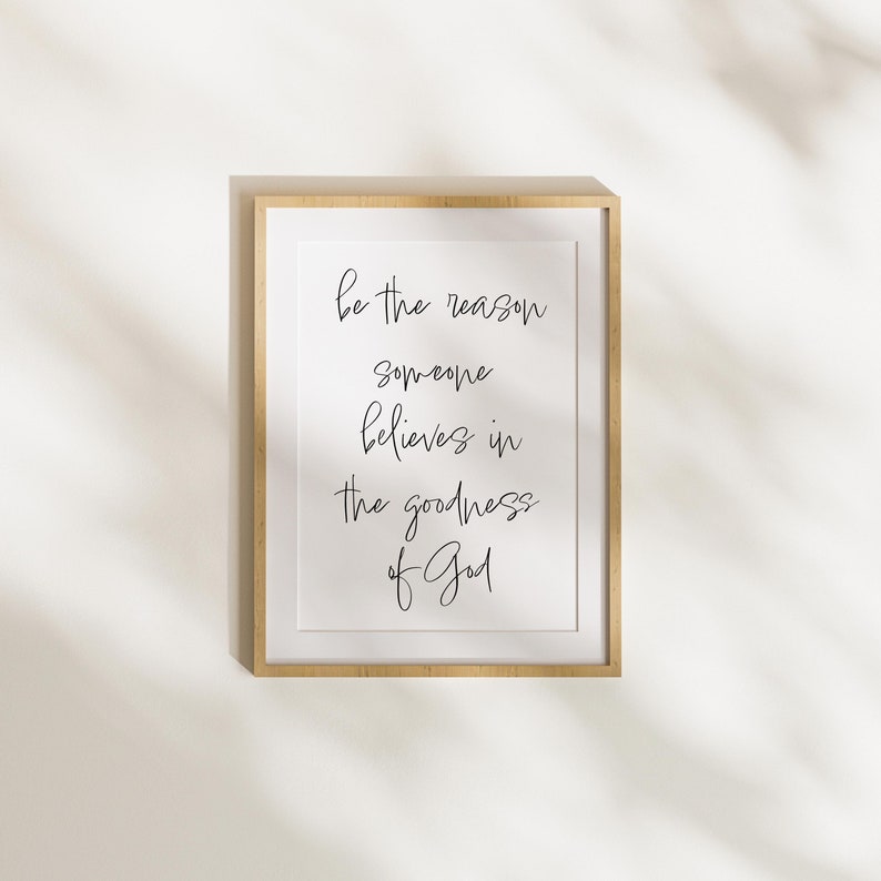 May include: A framed print with the text "Be the reason someone believes in the goodness of God" in black cursive writing on a white background.