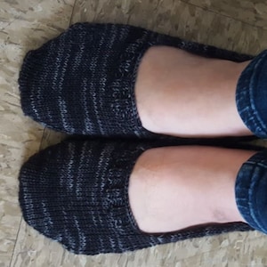 May include: A pair of black and grey striped knit socks with a subtle sheen. The socks are worn on a person's feet.