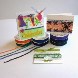 May include: Assortment of colorful ribbon trims and spools, including orange, green, blue, black, and purple. The ribbon trims are displayed on cards with various themes, including a birthday card with the word "Celebrated" and a Halloween card with a spider and the text "Happy Haunting".