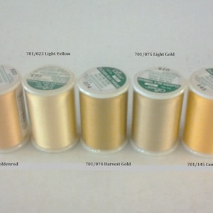 May include: Five spools of thread in various shades of yellow and gold. The spools are labeled with the numbers 701/023, 701/075, 701/029, 701/074, and 701/145. The thread colors are light yellow, light gold, goldenrod, harvest gold, and canary.