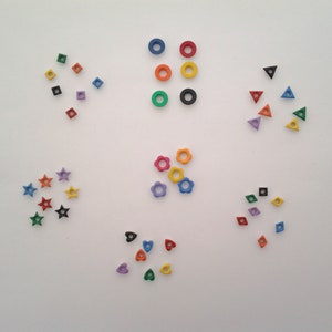May include: Assortment of colorful wooden buttons in various shapes, including circles, squares, stars, hearts, and flowers. The buttons are arranged in a circular pattern on a white background.