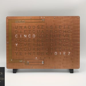 Puede incluir: Un WordClock de color cobre de StarkAllister. El reloj muestra la hora con palabras, con la palabra "CINCO" resaltada. El reloj rectangular tiene patas negras y un diseño de placa de circuito en el lado izquierdo.