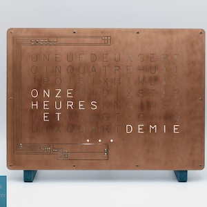 May include: A copper-colored clock with a unique design. The clock face features a grid of letters that spell out the time in French. The clock is on a stand with blue legs. The clock face reads "ONZE HEURES ET DIX QUART DE DEMIE".