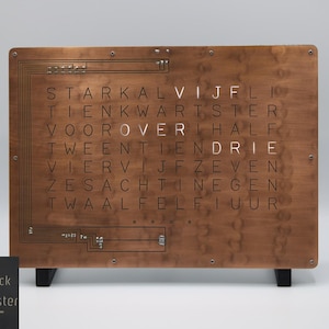 Op de afbeelding: Een houten woordklok met een koperen afwerking. De klok geeft de tijd weer met woorden in het Nederlands, zoals "half", "een", "twee", "drie", "vier", "vijf", "zes", "zeven", "acht", "negen", "tien", "elf", en "twaalf".