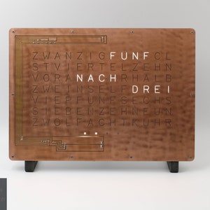 Pode incluir: Um relógio de parede de cobre com uma grade de palavras alemãs que soletram a hora. As palavras incluem "zwanzig", "funf", "viertel", "zehn", "vor", "nach", "halb", "zwei", "insel", "drei", "vier", "funf", "sechs", "sieben", "zehn", "neun", "zwolf", "acht", "kuhr".