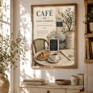Könnte beinhalten: Ein gerahmter Vintage-Print mit einer Pariser Cafészene. Das Kunstwerk enthält den Text "CAFÉ DE SAINT-GERMAIN" und zeigt einen Tisch mit Croissant, Kaffee und einer kleinen Tafelkarte. Eine Blumenvase und eine Zeitung sind ebenfalls zu sehen.