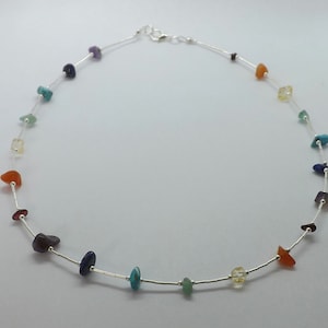 Könnte beinhalten: Eine silberne Kettenkette mit kleinen, bunten Edelsteinen. Die Steine sind in einem Regenbogenmuster angeordnet, mit roten, orangefarbenen, gelben, grünen, blauen, indigofarbenen und violetten Steinen.
