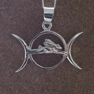 Puede incluir: Collar con colgante de plata con un símbolo de triple luna con una liebre estilizada corriendo por el centro.