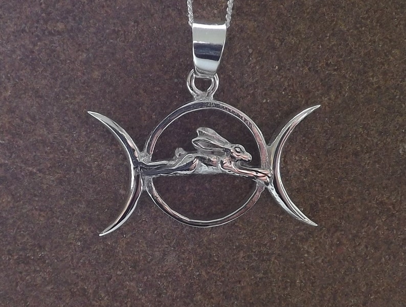 May include: Silver pendant necklace featuring a triple moon symbol with a stylized hare running through the center.